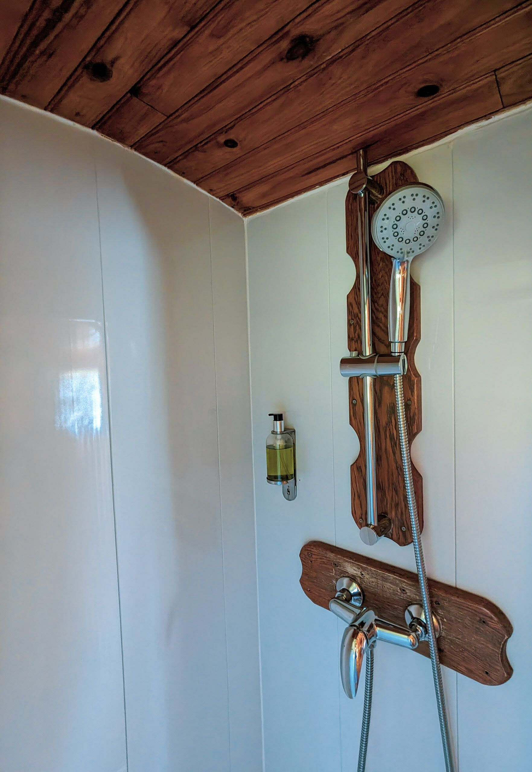 A shower with a wooden panel design, a handheld showerhead, and a soap dispenser.