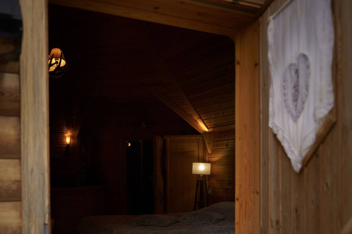 A cozy log cabin bedroom with a bed, a lamp, and a wooden ceiling.