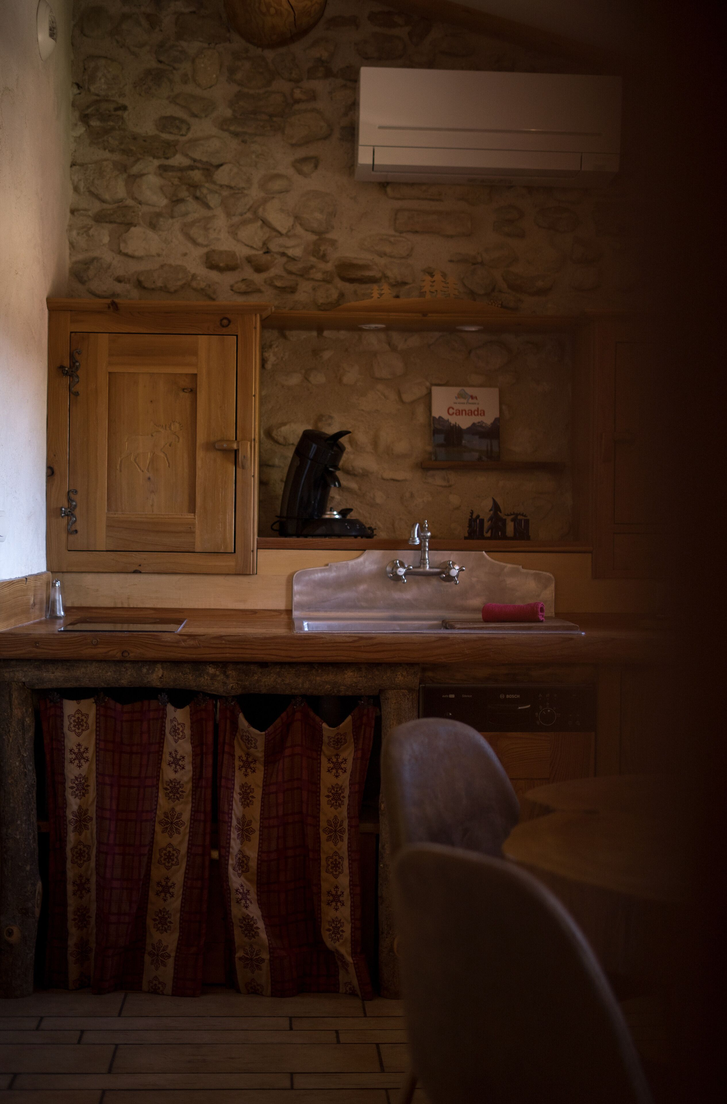 A rustic kitchen with a stone wall, wooden cabinets, a sink, and a stove.