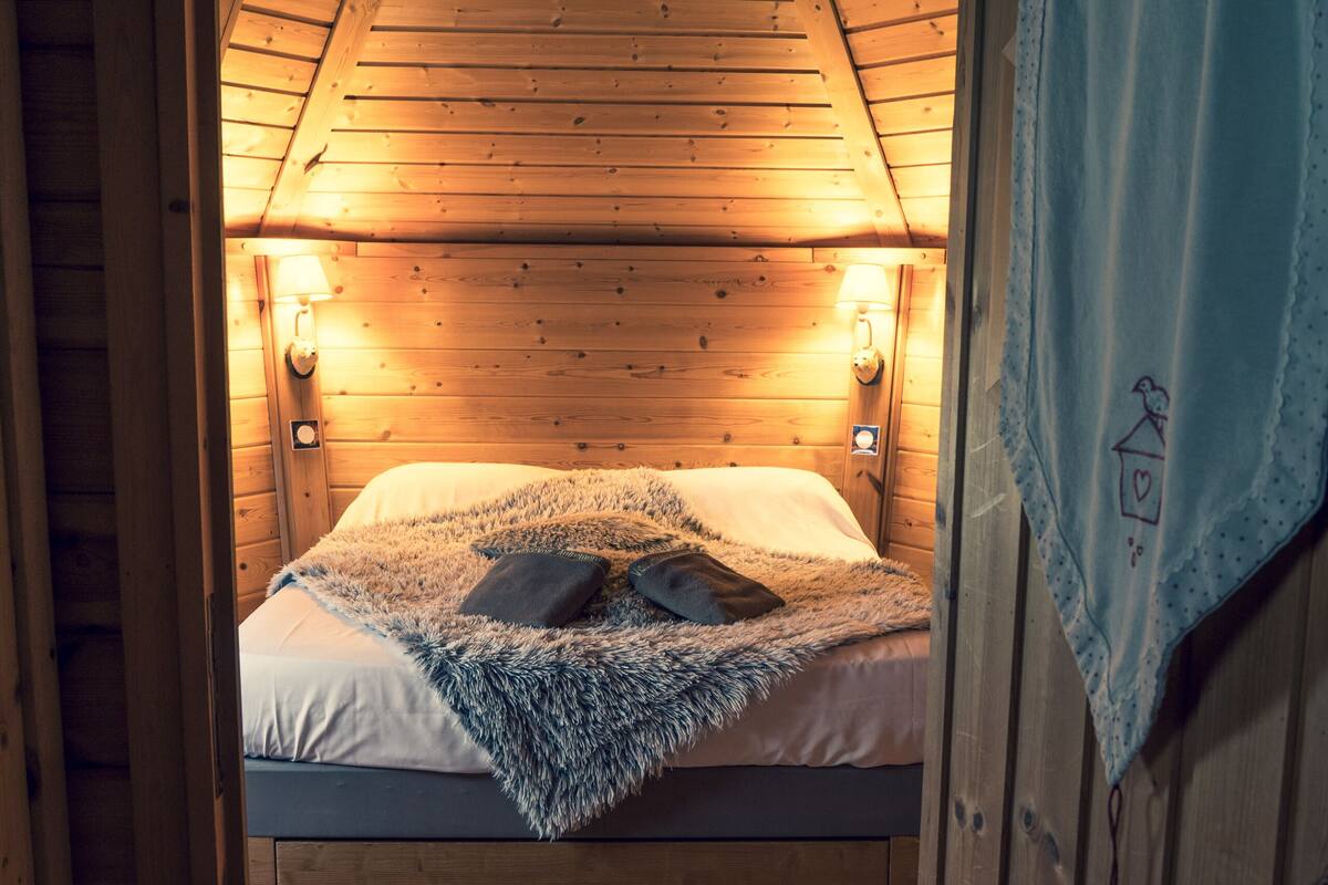 A cozy wooden cabin bedroom with a bunk bed, a fluffy blanket, and two wall-mounted reading lamps.