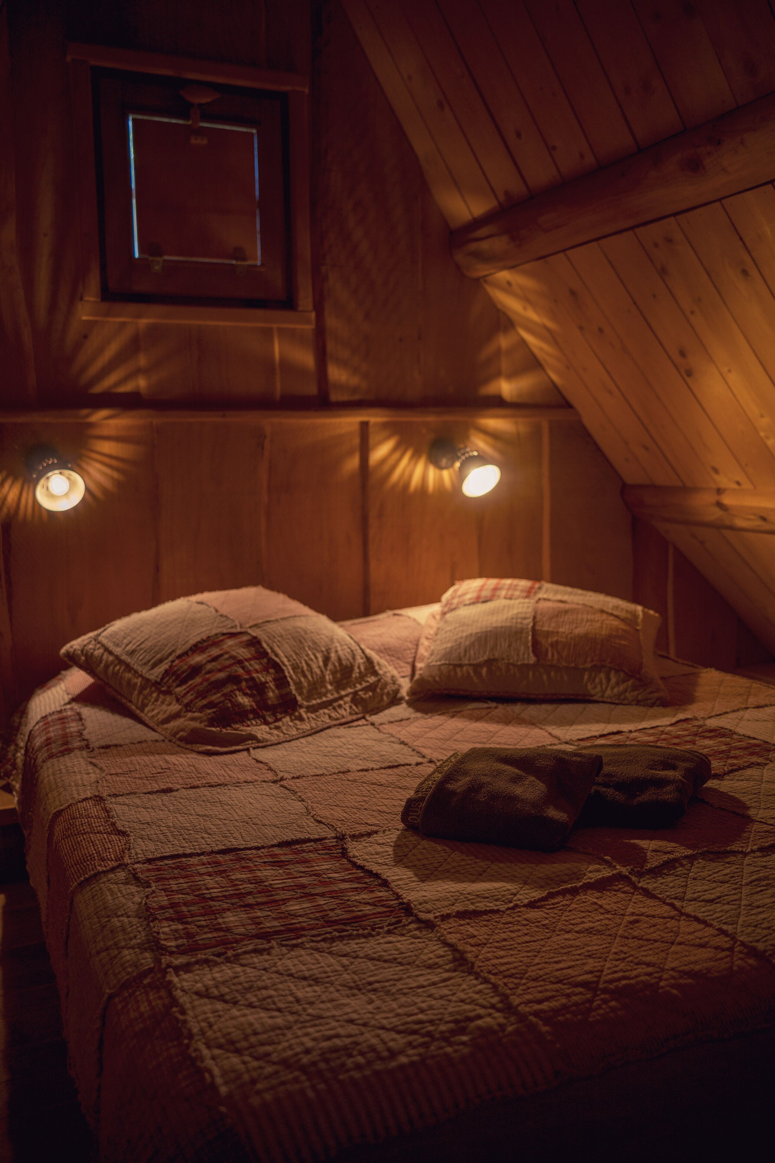 A cozy attic bedroom with a wooden ceiling, a quilted bedspread, and two bedside lamps.