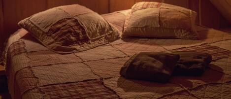 A cozy attic bedroom with a wooden ceiling, a quilted bedspread, and two bedside lamps.