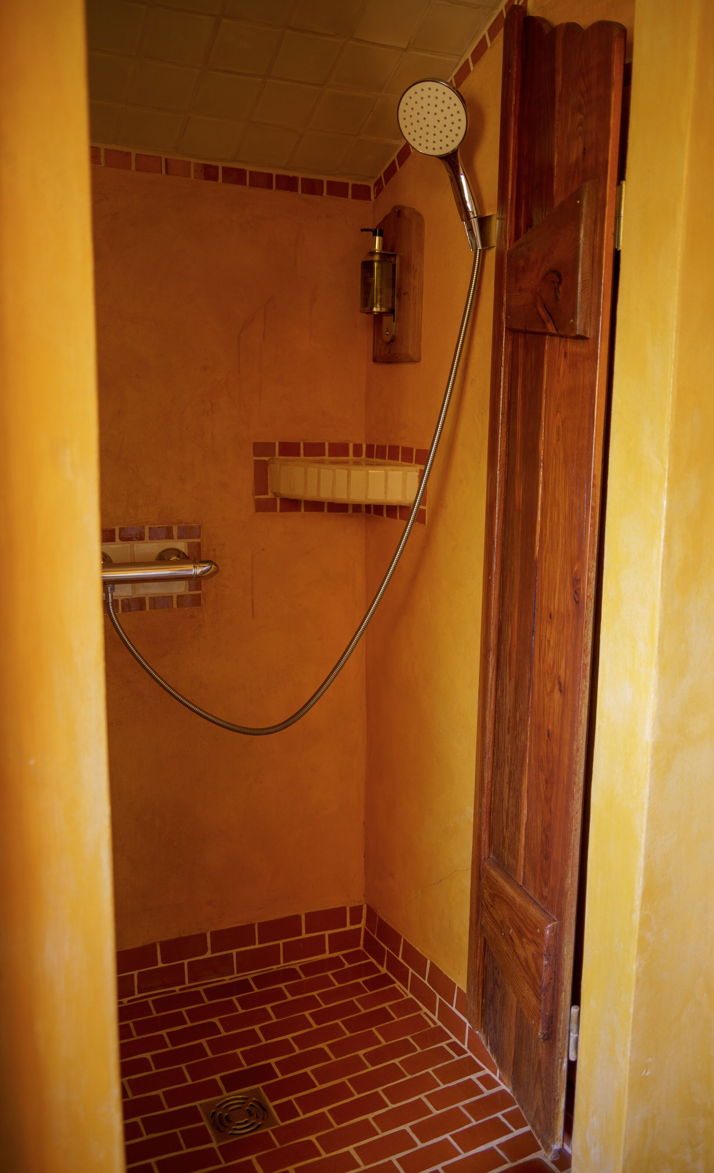 A shower area with a wooden door, a showerhead, and a tiled floor.