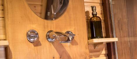 A stone basin sink with a wooden countertop, a wooden wall with a mirror, and a shelf with a bottle.