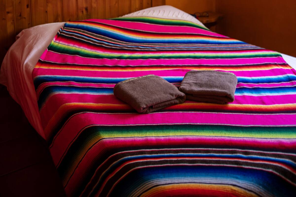 A room with a wooden headboard, a colorful striped bedspread, and a small painting on the wall.