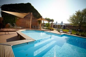 Piscina con muelle de madera y sillones de descanso, rodeada por una cabaña de madera y un área cubierta con dosel blanco.