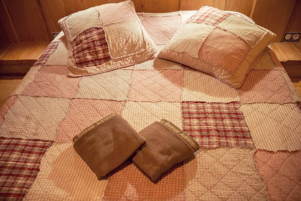 A bed with a quilted blanket and two pillows, a wooden headboard, and a bedside table with a radio.