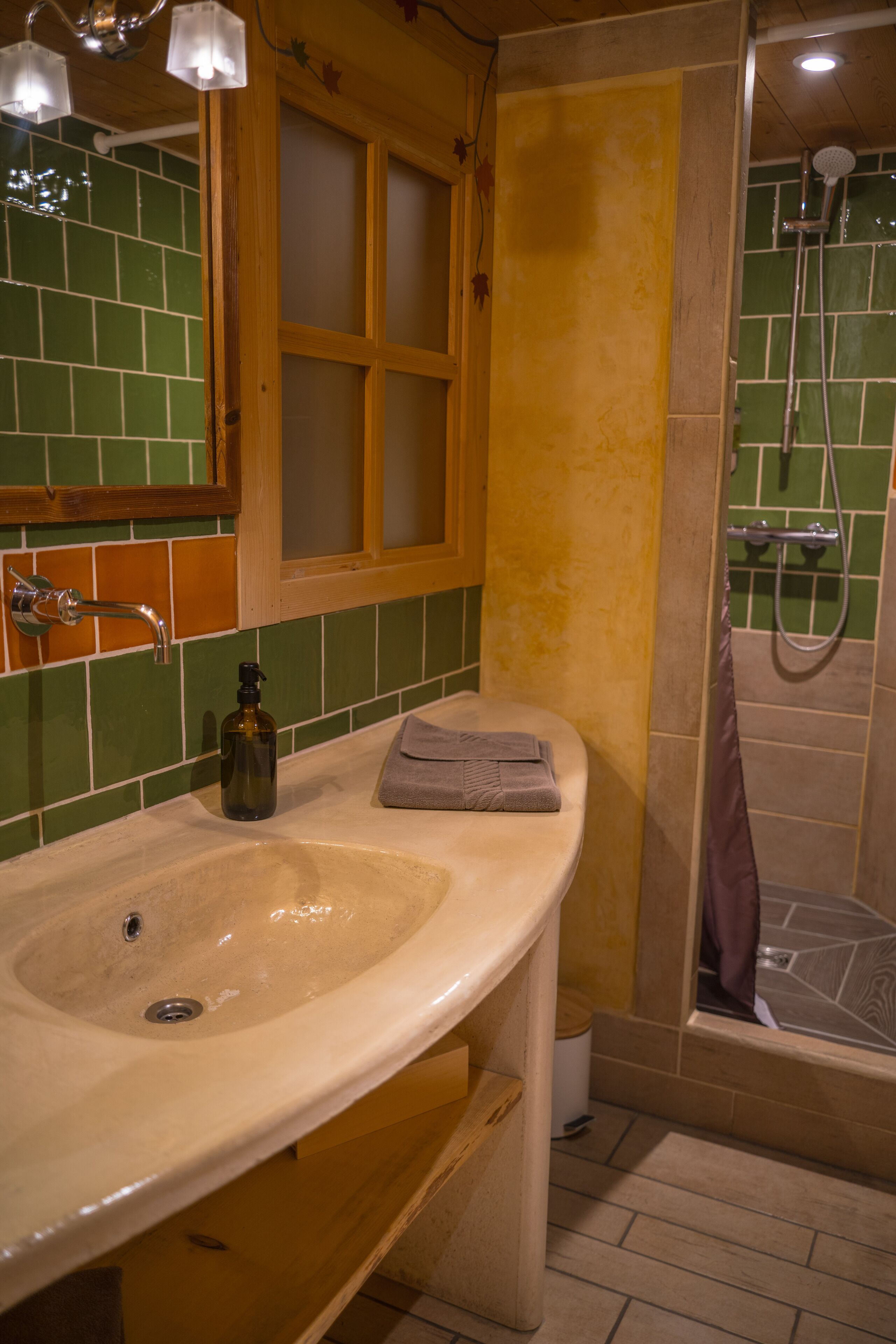 A bathroom with a beige sink, green and yellow tiled walls, a wooden cabinet, and a glass shower enclosure.
