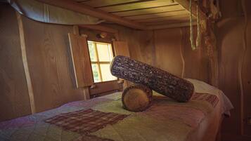 Una habitación rústica de madera con una cama, una ventana y una estufa sobre la cama.