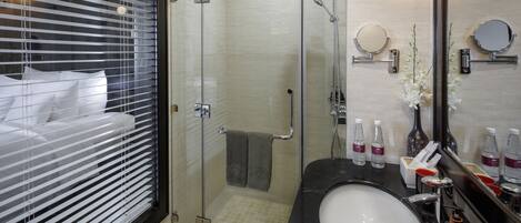 Un baño moderno con ducha de vidrio, lavamanos negro y un espejo grande.
