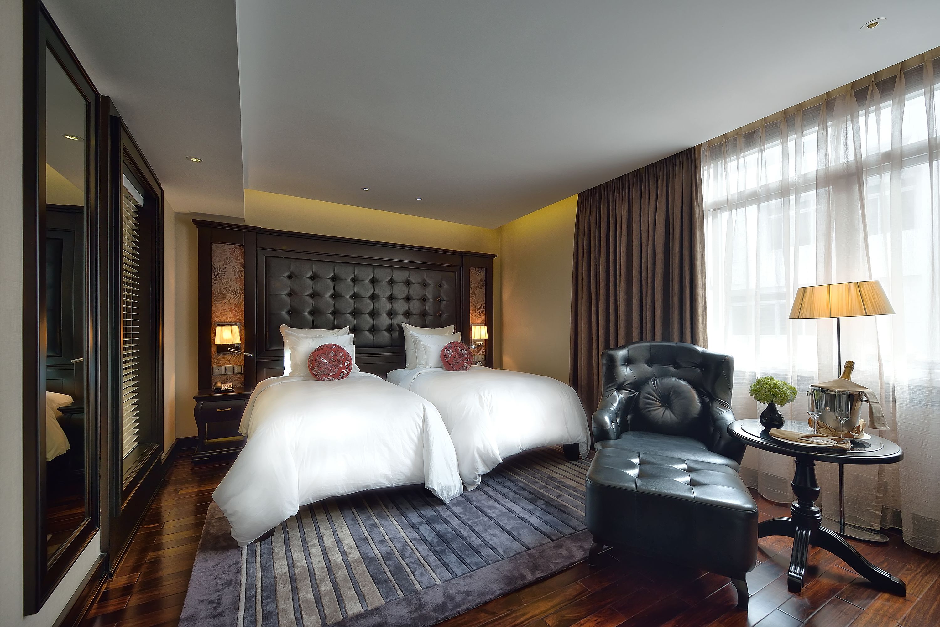 A hotel room with a large bed, a chair, a table with a lamp, and a mirror.