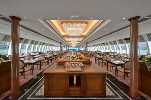 A luxurious dining area with a central buffet, elegant chandeliers, and large windows offering a view of the sea. - Paradise Suites Hotel (Ha Long)