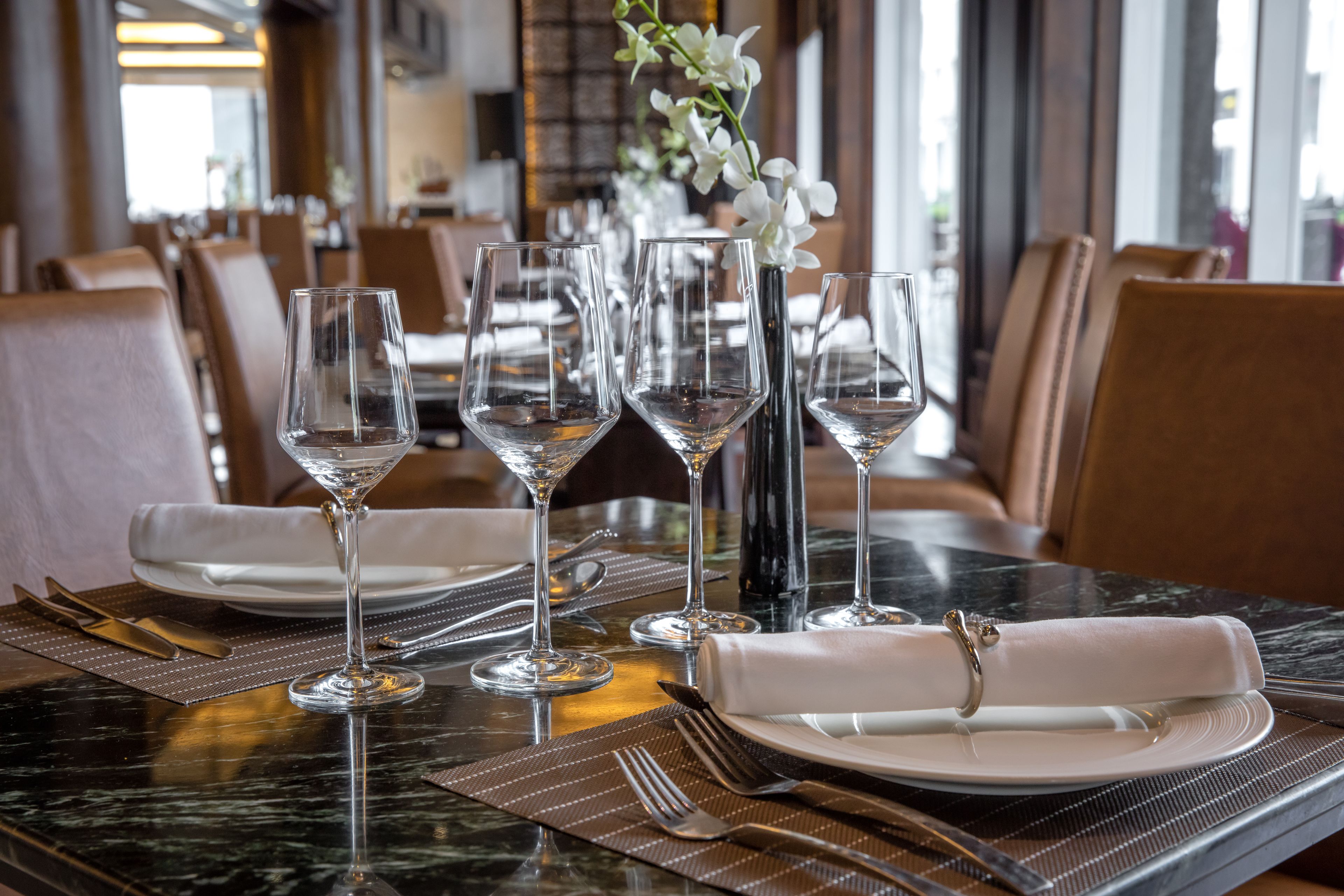 A dining table set with wine glasses, plates, and cutlery, with a vase of white flowers in the center.