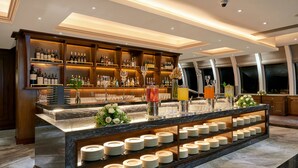 Een bar met drankflessen op planken, een marmeren aanrecht met borden en een decoratieve vaas met bloemen.