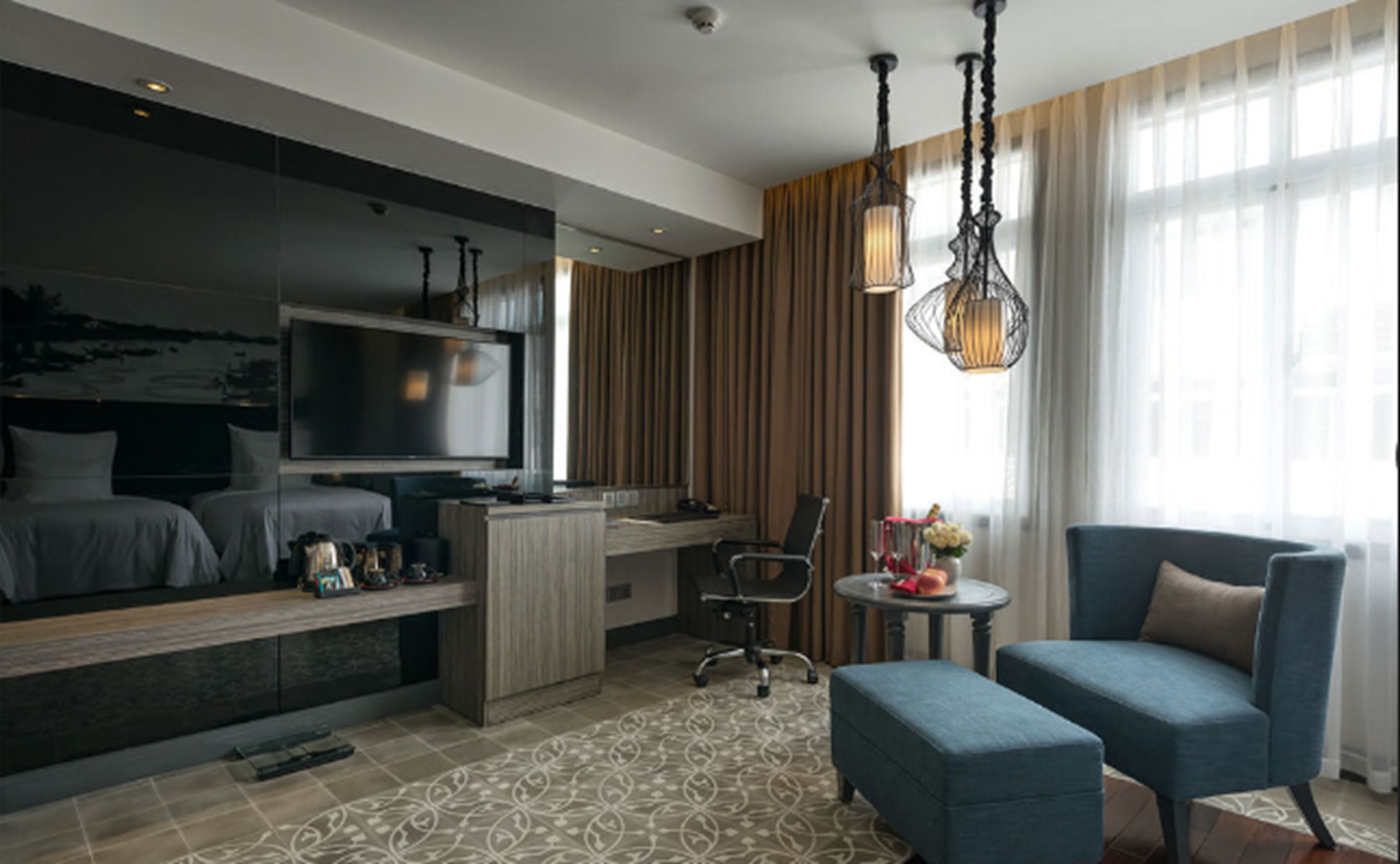 Ein modernes Hotelzimmer mit Bett, Schreibtisch, Fernseher und einer Sitzecke mit Sessel und Hocker.