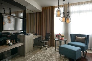 A modern hotel room with a flat-screen TV, a desk with a computer, a chair, a sofa, and a decorative table with flowers. - Paradise Suites Hotel (Ha Long)