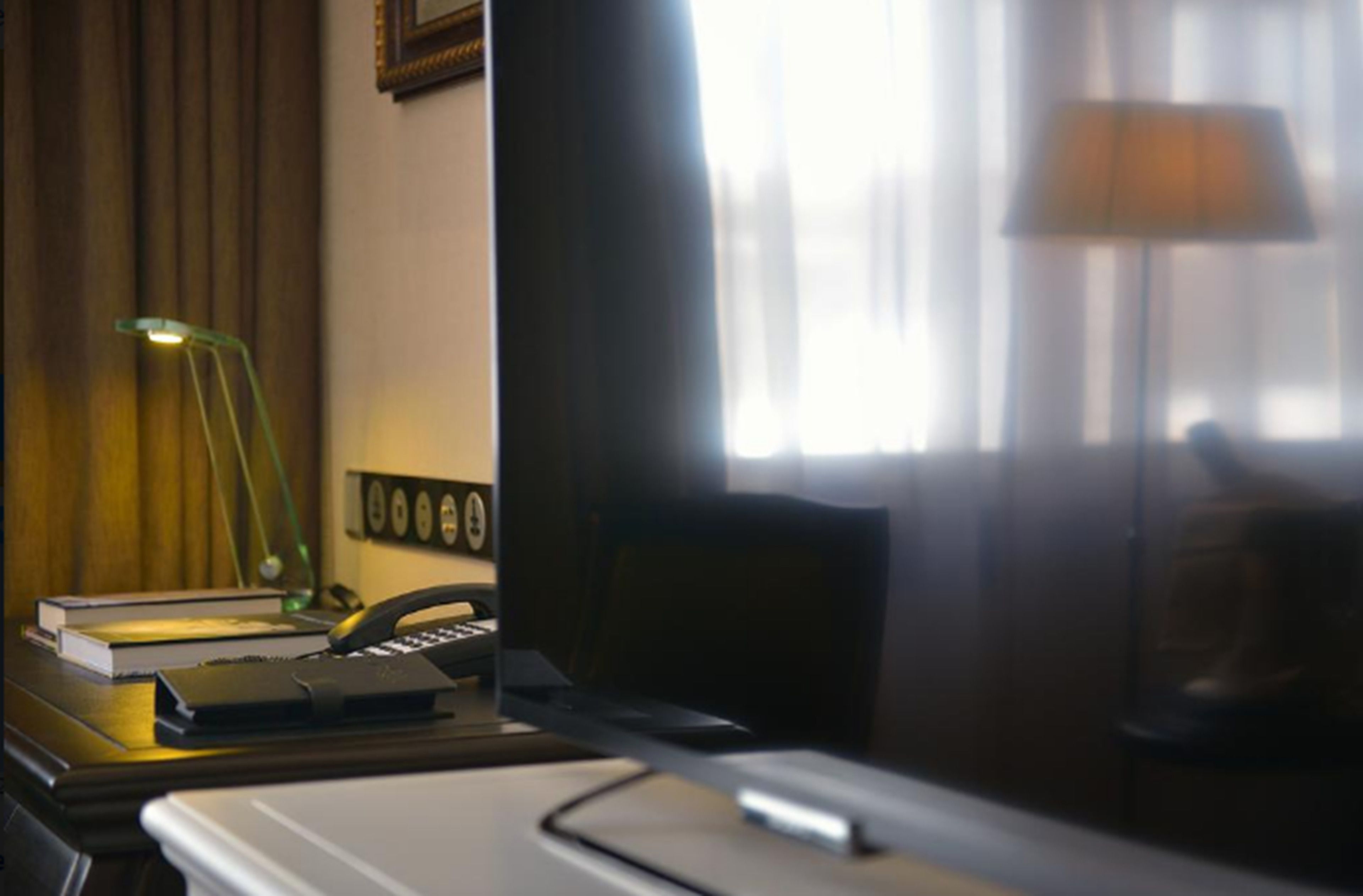A hotel room with a desk, lamp, books, and a telephone.