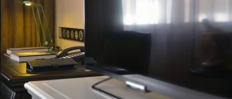 A hotel room with a desk, lamp, books, and a telephone.