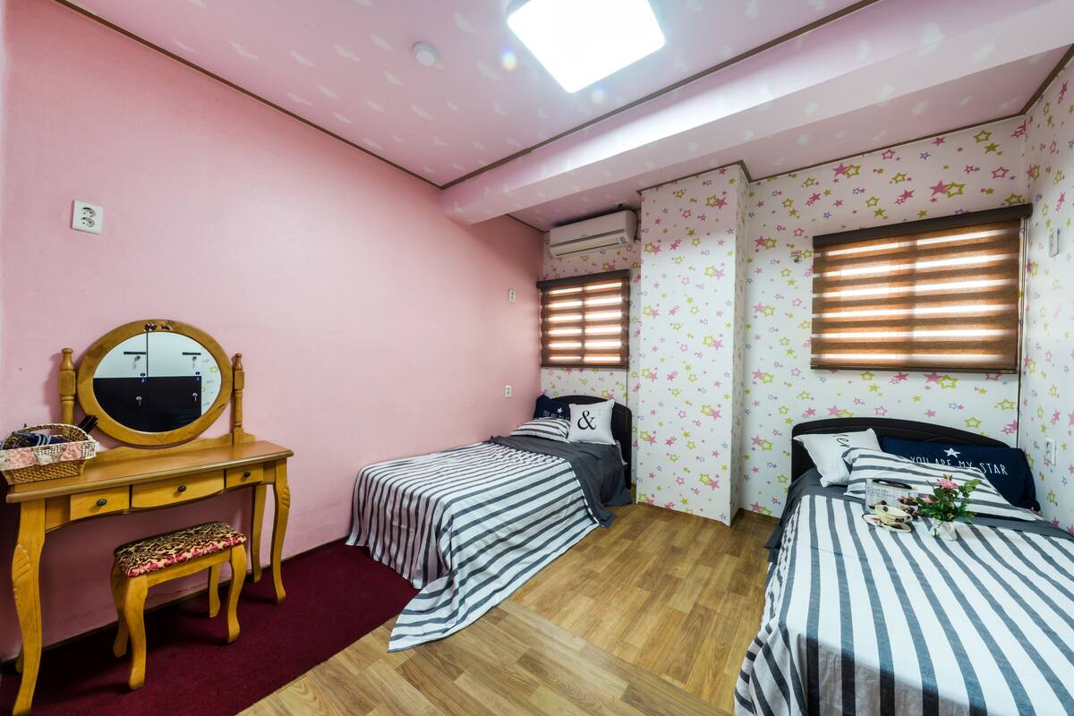 A bedroom with two single beds, a wooden desk with a mirror, and a red carpet.