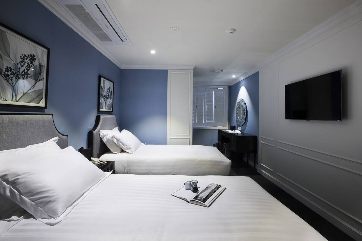 A hotel room with two beds, a flat-screen TV, a bedside table with a lamp, and framed artwork on the walls.