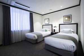A hotel room with two beds, a large window with curtains, an air conditioning unit, and framed artwork on the walls.