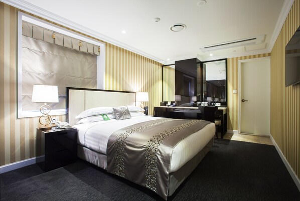 A hotel room with a large bed, bedside tables, a desk, a mirror, and a wardrobe.