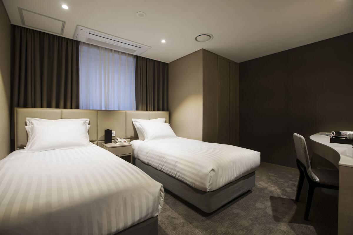 A hotel room with two beds, a desk, and a chair.