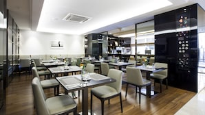 A modern restaurant with wooden flooring, neatly arranged tables and chairs, and a black wall with a decorative panel.