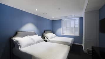 A hotel room with two beds, a window with blinds, a flat-screen TV, and a ceiling air vent.