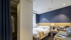A hotel room with a bed, bedside table, desk, laptop, and a window.