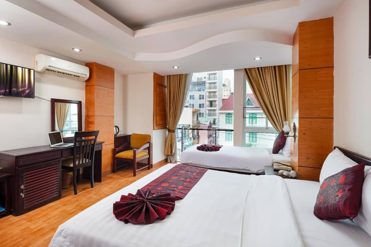 A hotel room with a bed, a desk with a laptop, a chair, and a view of buildings through the window.