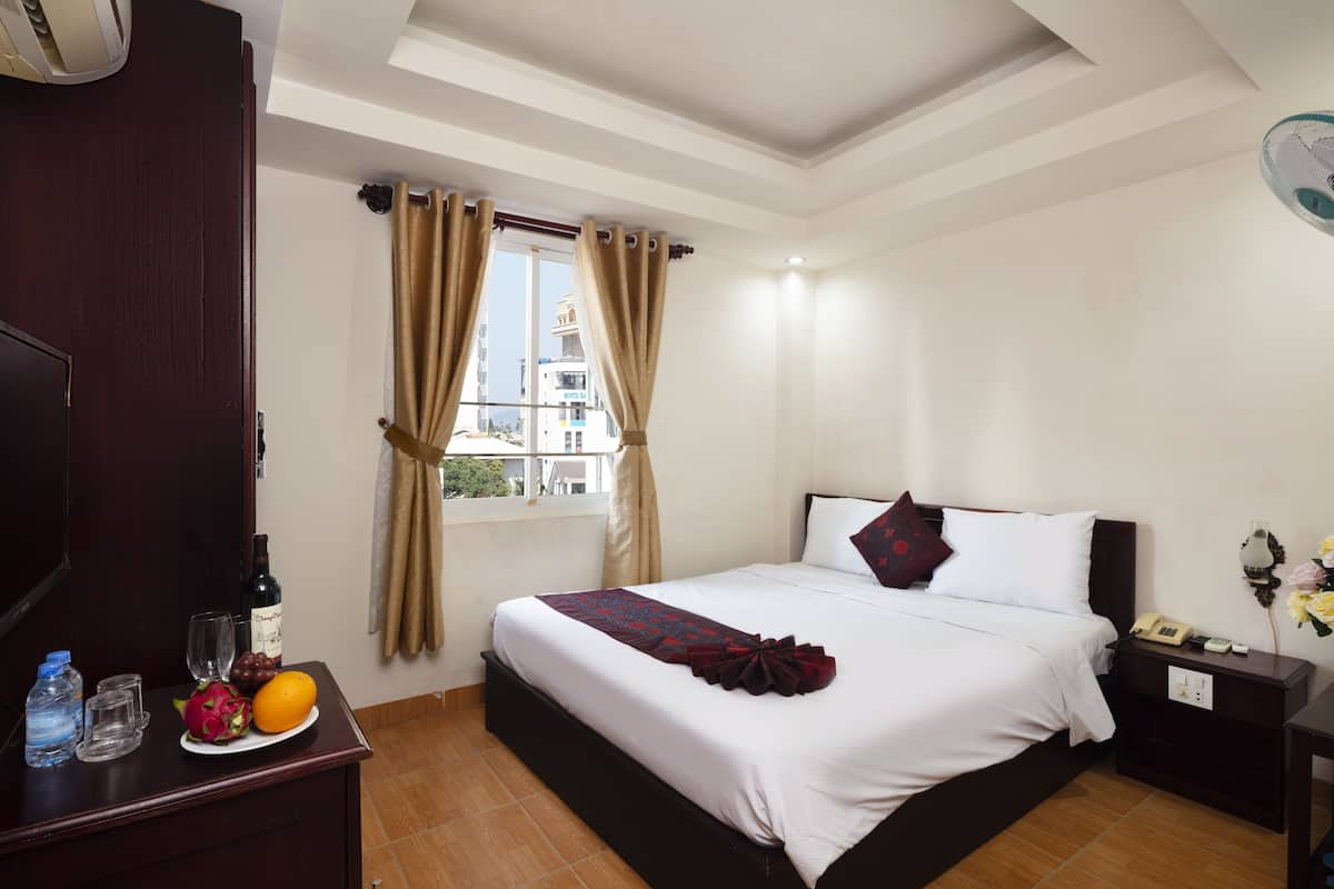 A hotel room with a bed, bedside table, and a window with curtains.
