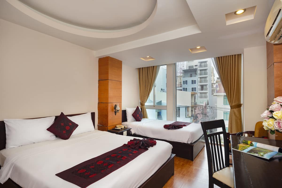 A hotel room with two beds, a wooden headboard, a desk with a chair, and a large window with curtains.