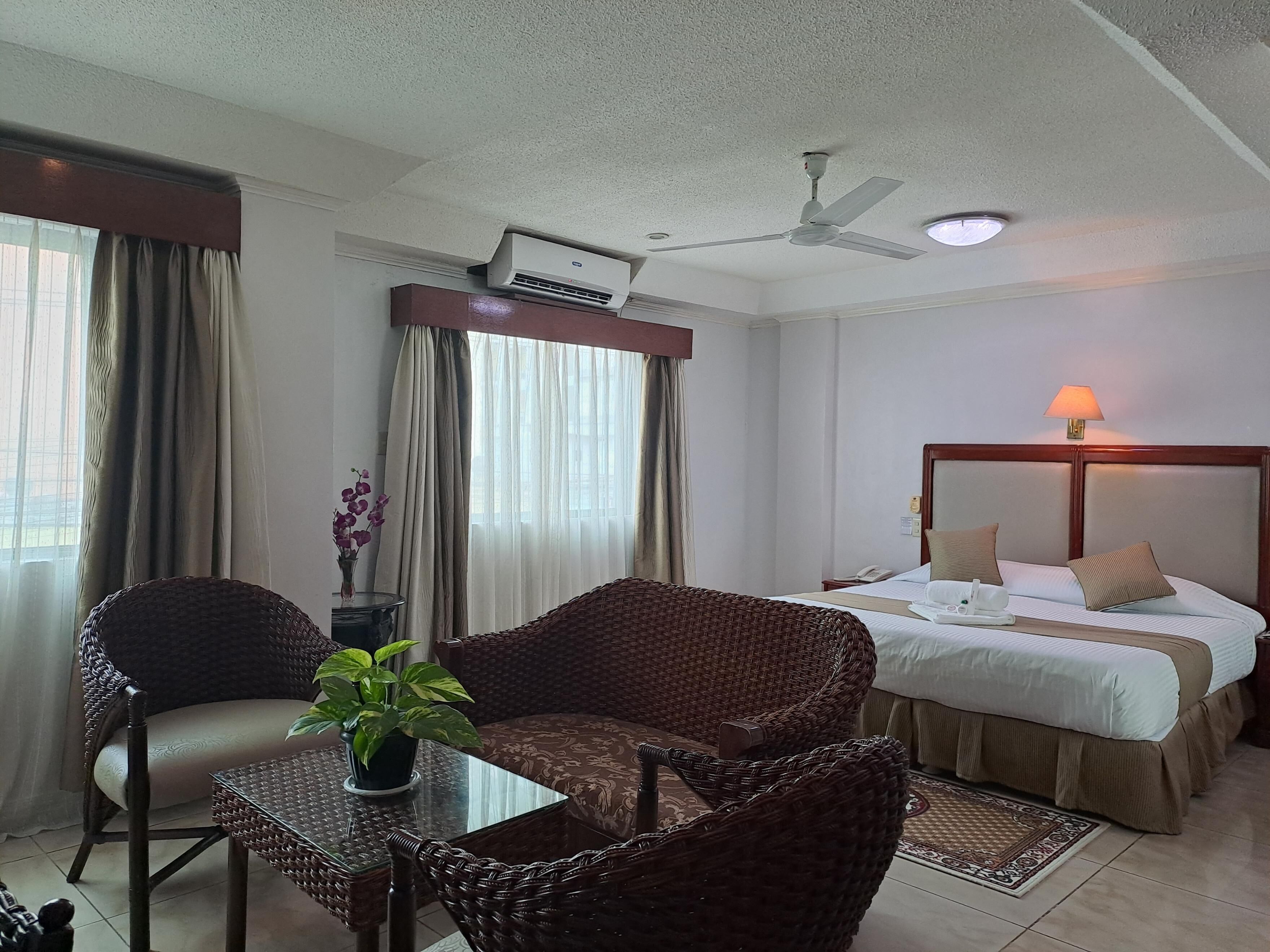 A hotel room with a bed, a table with chairs, a ceiling fan, and a window with curtains.