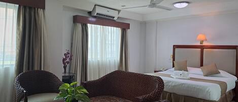 A hotel room with a bed, a table with chairs, a ceiling fan, and a window with curtains.