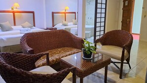 Une chambre d’hôtel avec deux lits, des fauteuils en osier, une table en verre et une plante en pot.