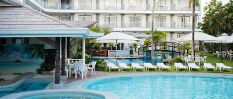 A hotel pool area with lounge chairs, umbrellas, and a view of the building.