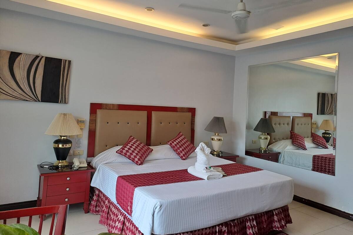 A hotel room with a large bed, a ceiling fan, and a mirror.
