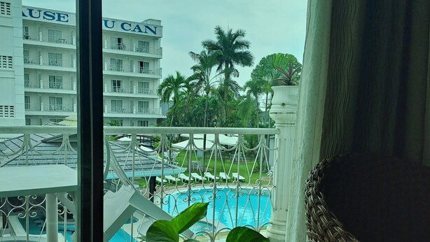 A hotel room with a view of a swimming pool, a balcony with a potted plant, and a building with balconies in the background.