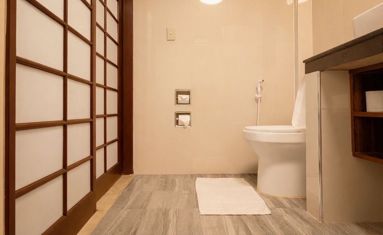 A bathroom with a toilet, a towel, a wooden partition, and a light fixture.