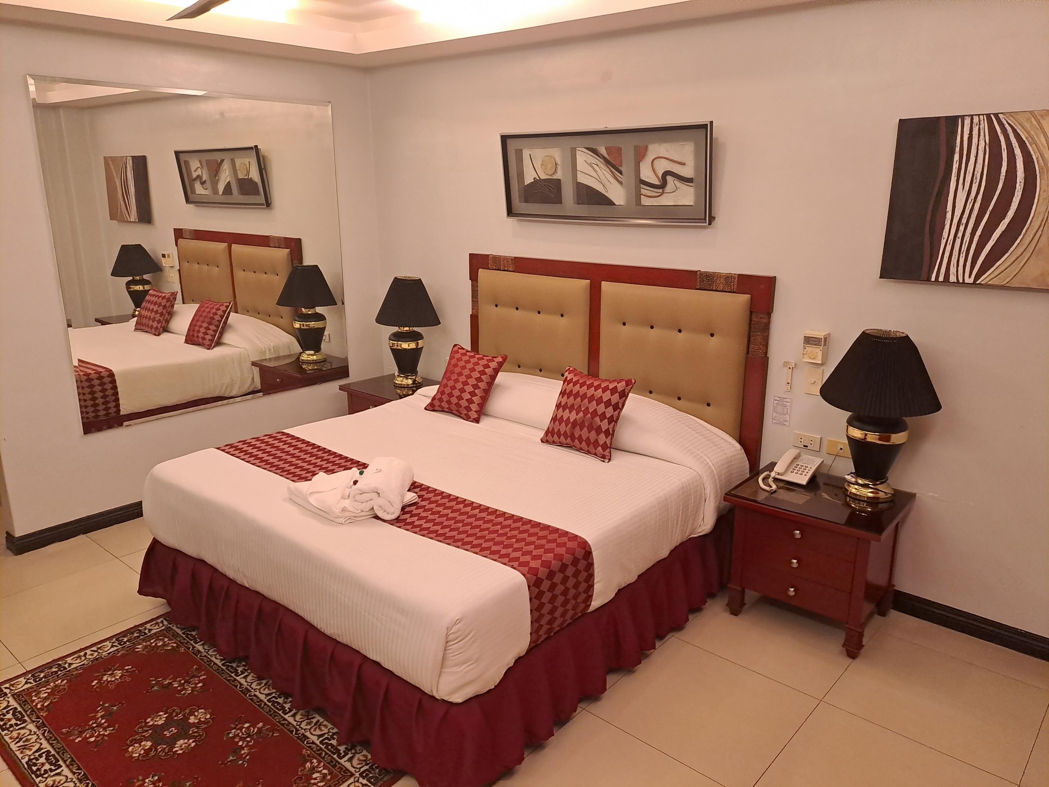 Una habitación de hotel con una cama grande, una mesita de noche con lámpara, un espejo y obras de arte en las paredes.