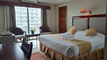 A hotel room with a bed, two chairs, a desk, and a view of a building through the window.