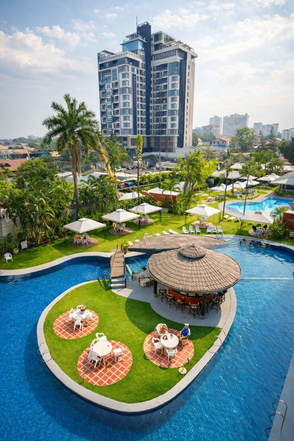 A hotel with a swimming pool, outdoor seating, and a view of a tall building in the background.