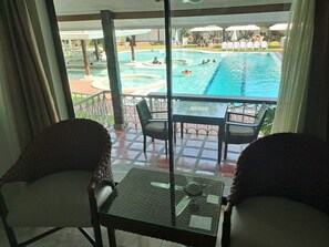 A balcony with wicker chairs and a glass table overlooking a swimming pool area with lounge chairs and umbrellas. - Wild Orchid Resort (Angeles City)