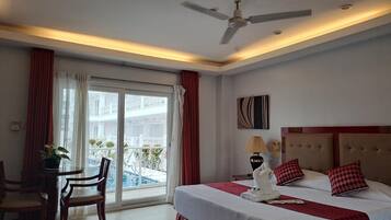 A hotel room with a bed, a ceiling fan, a table with chairs, a lamp, and a view of the outside balcony.