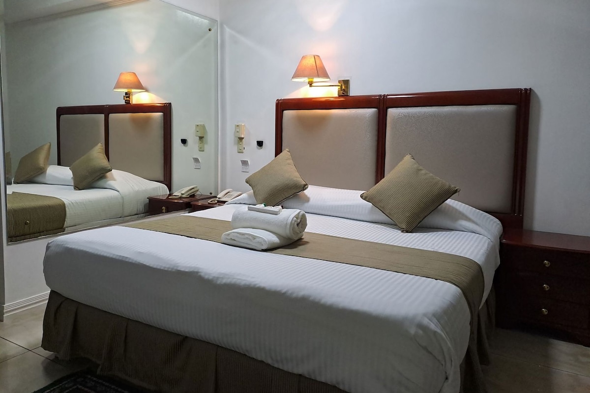 A hotel room with two beds, a large mirror, bedside lamps, a telephone, and a bedside table.