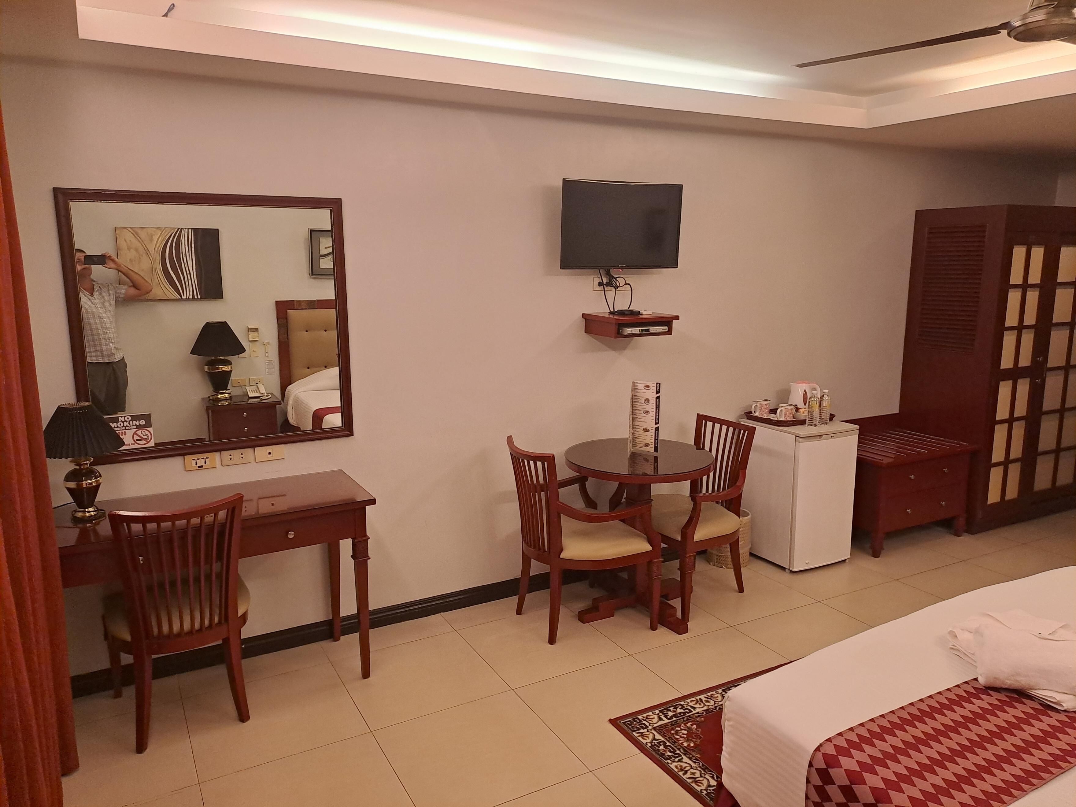Habitación de hotel con cama, escritorio, silla, televisión y una mesita con control remoto.