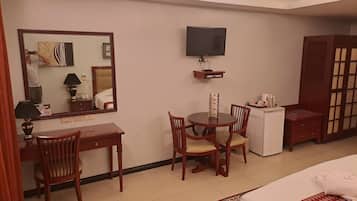 Habitación de hotel con cama, escritorio, silla, televisión y una mesita con control remoto.