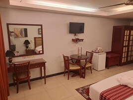 Habitación de hotel con cama, escritorio, silla, televisión y una mesita con control remoto.
