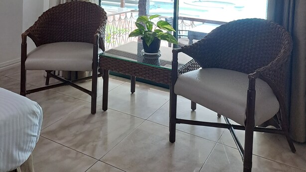 Une pièce avec deux fauteuils en osier, une table en verre et une plante en pot.
